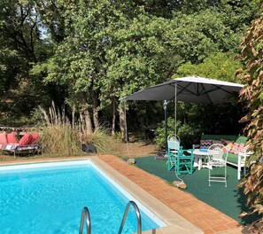 A swimming pool with a brick border, surrounded by a patio area with outdoor furniture and a covered seating area.