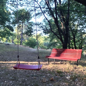 Un banco rojo y un conjunto de columpios en un parque con árboles y césped.