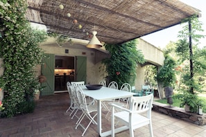 Eine Terrasse im Freien mit Tisch und Stühlen, einem Reetdach und viel Grün.
