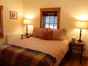 Een knus slaapkamer met een groot bed, twee bedlampjes, een raam met houten kader, en een radiator.