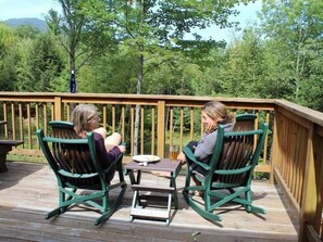 Deux fauteuils à bascule sont placés sur une terrasse en bois, avec une table entre eux.