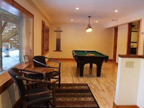 A billiards room with a pool table, wooden chairs, and a hanging light fixture. - Large Log Cabin in the Heart of the ADKS (Keene)