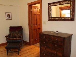 A room with a wooden door, a dark wooden dresser, a patterned armchair, and a framed mirror on the wall.