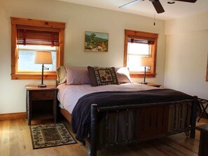 A bedroom with a wooden bed, two bedside tables with lamps, a rug, and a painting on the wall.