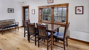 A dining area with a wooden table and chairs, a bench, and a window with a view of trees. - Large Log Cabin in the Heart of the ADKS (Keene)