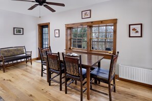 A dining area with a wooden table and chairs, a bench, and a window with a view of trees.