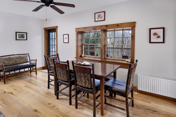 A dining area with a wooden table and chairs, a bench, and a window with a view of trees.