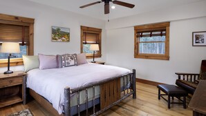 Una camera da letto con un letto in legno, due comodini con lampade, una ventola a soffitto e ampie finestre con stipiti in legno.