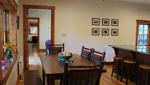 A dining area with a wooden table, chairs, and a bar with stools. - Large Log Cabin in the Heart of the ADKS (Keene)