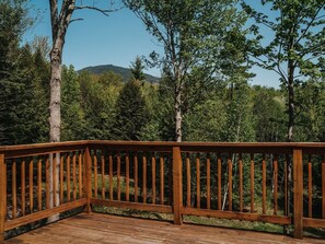A wooden deck with a railing, surrounded by trees and a mountain in the background. - Large Log Cabin in the Heart of the ADKS (Keene)