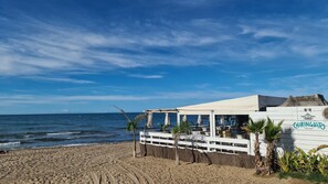 Um restaurante à beira-mar com fachada branca, mesas ao ar livre e vista para o oceano.
