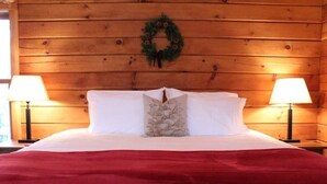Una cama con cubrecolcha rojo, almohadas blancas y una almohada decorativa. Hay dos lámparas a cada lado de la cama.