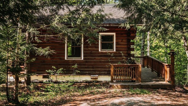 A log cabin with a wooden deck and a staircase leading to the entrance. - Honeymoon Cabin with Jacuzzi Tub (Keene)