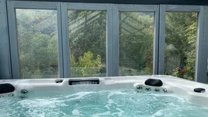 A hot tub with a view of a garden through large windows.