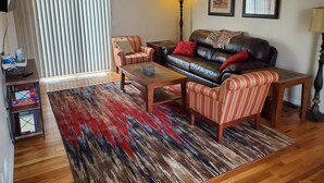 Una sala de estar con un sofá, sillones, una mesa de centro, un tapete estampado y una lámpara.