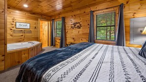 A wooden cabin bedroom with a large bed, a wooden bathtub, and a window with curtains. - Leconte Lookout - Stunning Views - Hot Tub - Games (Sevierville)
