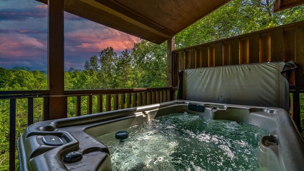A hot tub with a wooden deck and railing, surrounded by lush greenery and a scenic view. - Leconte Lookout - Stunning Views - Hot Tub - Games (Sevierville)