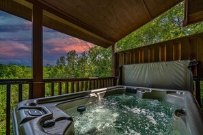 A hot tub with a wooden deck and railing, surrounded by lush greenery and a scenic view. - Leconte Lookout - Stunning Views - Hot Tub - Games (Sevierville)