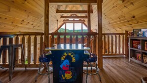 A wooden interior with a central table featuring a cartoon character, surrounded by metal stools. - Leconte Lookout - Stunning Views - Hot Tub - Games (Sevierville)