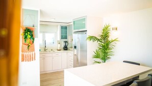Una cocina moderna con armarios blancos, un refrigerador de acero inoxidable y una cafetera. Hay una planta en la encimera y piso de madera.