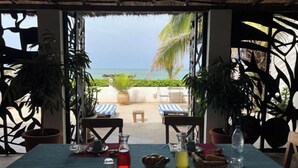An outdoor dining area with a view of the beach and ocean, featuring a table set with various dishes and drinks.