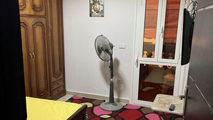 Quarto com cama, ventoinha, guarda-roupa, porta com janela e chão em azulejo.