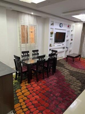 A dining area with a glass-top table and chairs, a patterned carpet, and a television on a white wall. - central/nice area (محافظة القاهرة‬)
