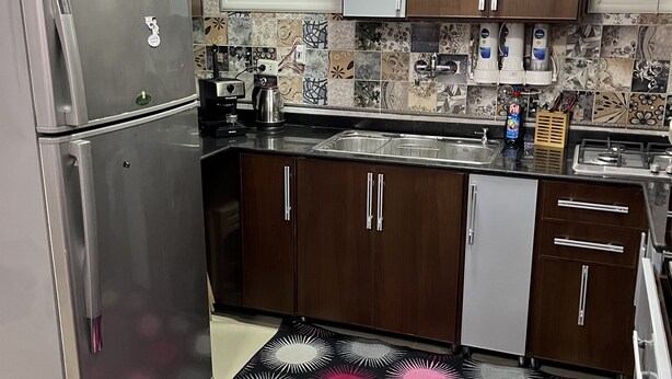 Uma cozinha moderna com eletrodomésticos de aço inoxidável, armários de madeira, painel de fundo padronizado e um tapete preto e rosa.