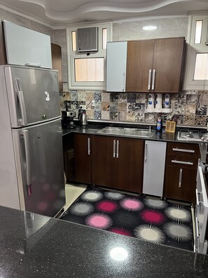 Una cuina moderna amb electrodomèstics d'acer inoxidable, armaris de fusta, un frontó amb un disseny decoratiu i una catifa negra i rosa.