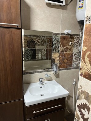 Un baño con un lavamanos blanco, un espejo y azulejos estampados.