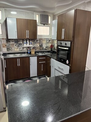 Una cocina moderna con armarios de madera oscura, encimera de granito negro, horno empotrado y ventana sobre el fregadero.