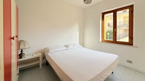 Una camera da letto con un letto, un comodino, una lampada, una finestra che dà su edifici e una porta.