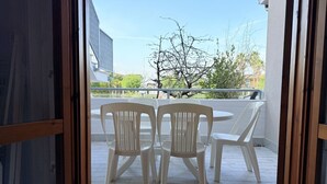 Un balcone con sedie e tavolo di plastica, un recinto bianco e un albero sullo sfondo.