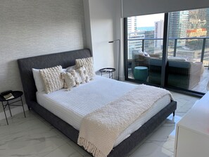 Relax in a spacious bedroom with a large bed, side table, and city views.