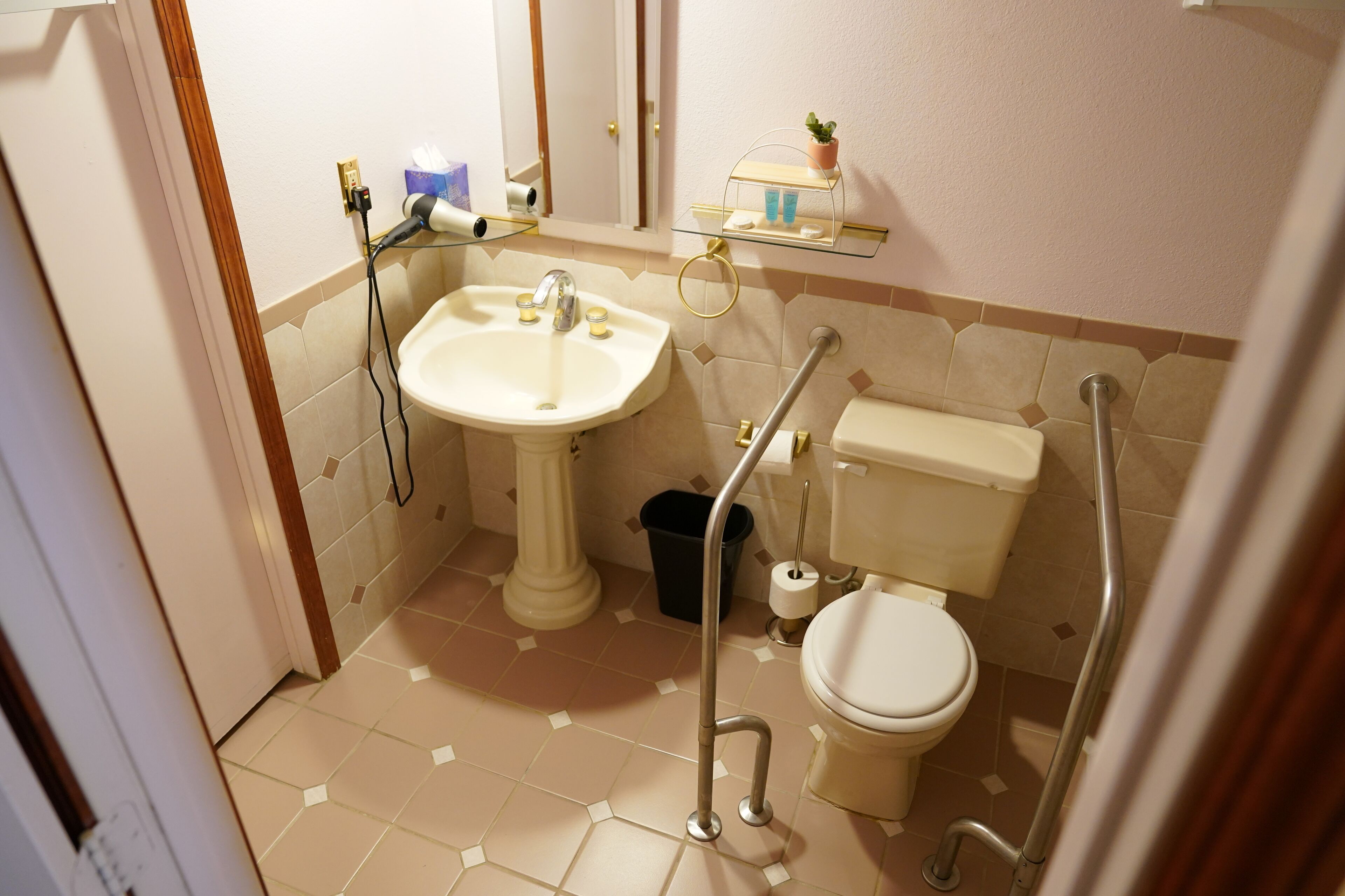 A bathroom with a pedestal sink, toilet, and grab bars.