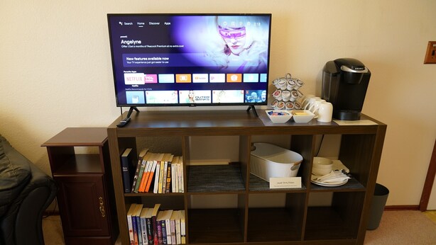 Un salon avec un téléviseur à écran plat posé sur un meuble en bois, une machine à café et une bibliothèque remplie de livres.