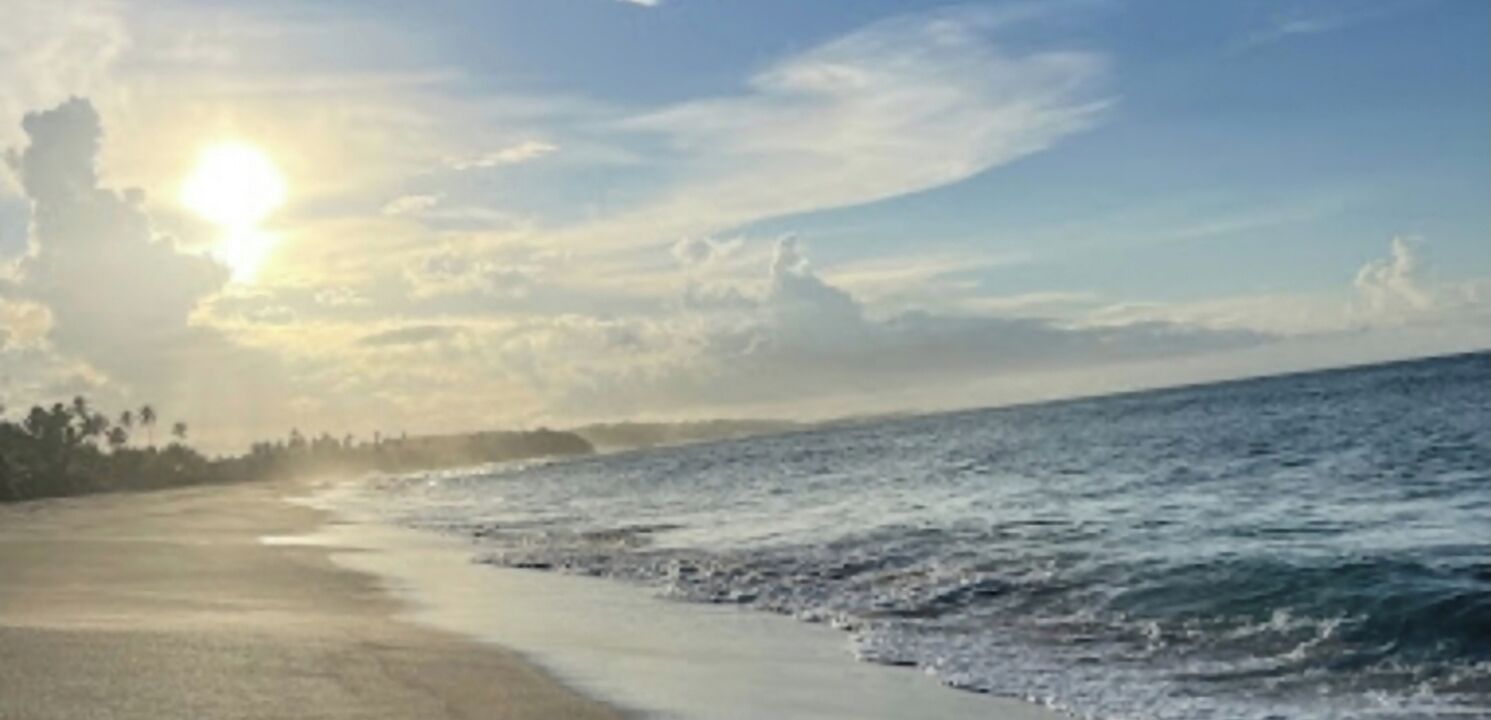 Ein Strand mit blauem Himmel und Sonnenlicht, das sich im Wasser spiegelt.