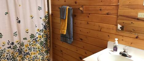 A bathroom with wooden walls, a toilet, a sink with a mirror, and a shower curtain with floral patterns.