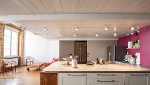 A modern kitchen with a large island, wooden chairs, a dining table, and a view of the city through a large window.