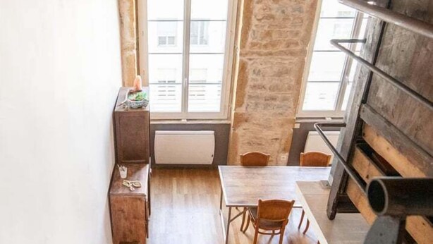 A narrow staircase leading to a dining area with a wooden table and chairs, a window, and a stone wall.