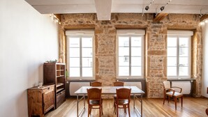 A room with a stone wall, wooden floor, a table with chairs, a radiator, and a wooden cabinet.