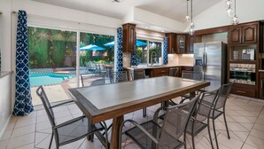Une cuisine moderne dotée d’un grand îlot central, d’appareils électroménagers en acier inoxydable et offrant une vue sur une piscine et un espace patio.