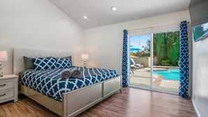Une chambre à coucher avec un lit, des tables de chevet et une vue sur une piscine, visible à travers une porte vitrée.