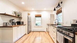 A modern kitchen with wooden flooring, white cabinetry, a built-in oven, a stove, and a window with a view. - Modern Mountain Getaway with Fire Pit (Shandaken)