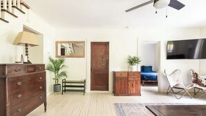 A living room with a wooden dresser, a lamp, a mirror, a blue sofa, a TV, and a ceiling fan. - Modern Mountain Getaway with Fire Pit (Shandaken)