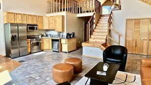 A spacious kitchen with wooden cabinets, a stainless steel refrigerator, and a coffee maker. There is a staircase leading to a loft area with a wooden railing. - The Stargazer-Your private retreat in the mountains! (Crestone)