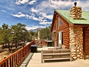 A log cabin with a stone chimney, a deck with outdoor furniture, and a view of trees and mountains. - The Stargazer-Your private retreat in the mountains! (Crestone)