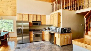 A modern kitchen with wooden cabinets, stainless steel appliances, and a stone tile floor. - The Stargazer-Your private retreat in the mountains! (Crestone)