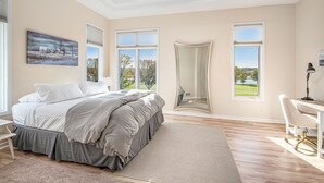 Une chambre à coucher avec un grand lit, un bureau et une vue sur l’extérieur par les fenêtres.