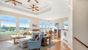 Un salon spacieux doté d’une grande fenêtre, d’un ventilateur de plafond et d’un coin repas offrant une vue sur l’extérieur.